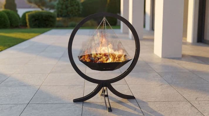 Modern outdoor fire pit with flames, set on a stone patio in a landscaped garden.