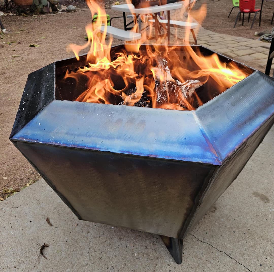 Modern hexagonal fire pit with vibrant flames and logs burning inside, set outdoors.