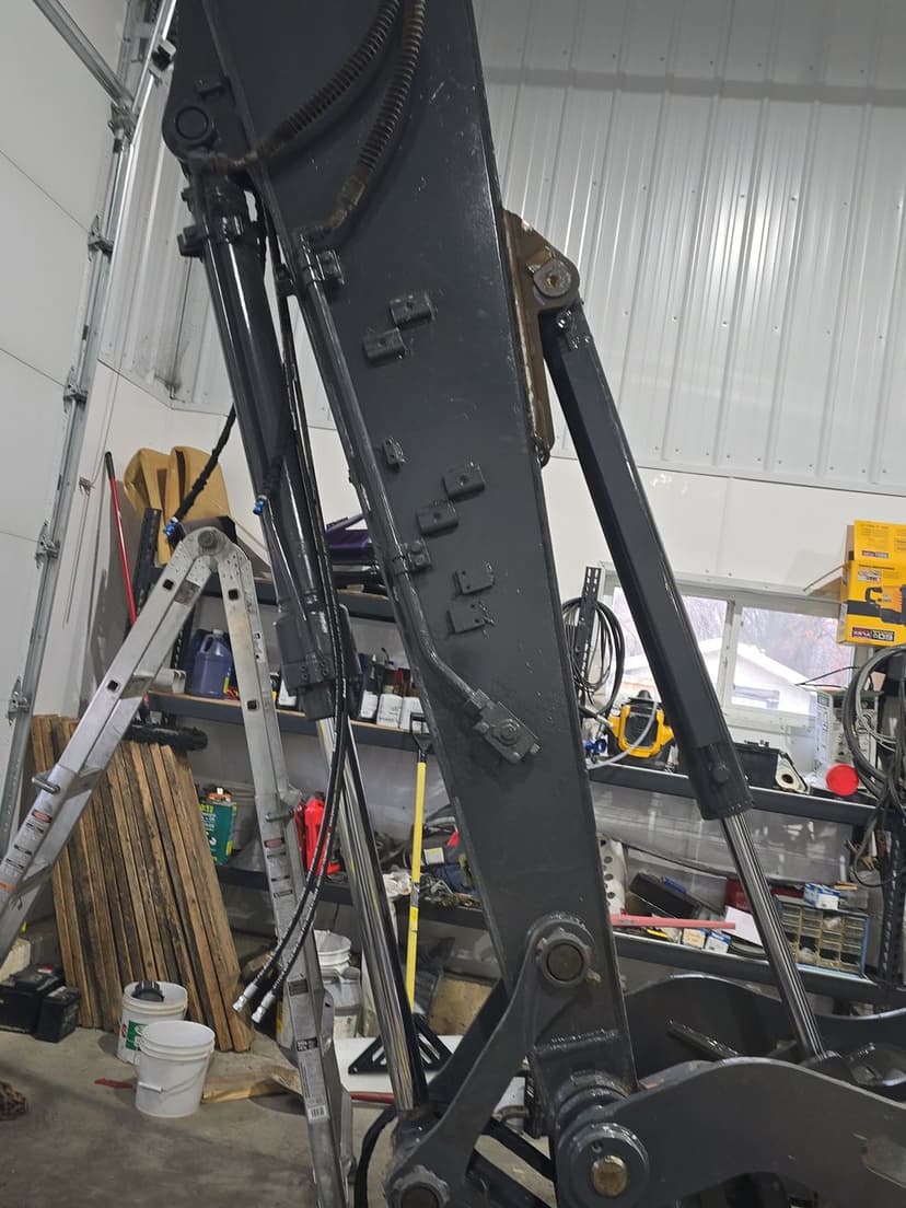 Heavy machinery excavator arm with hydraulic components in a workshop setting.