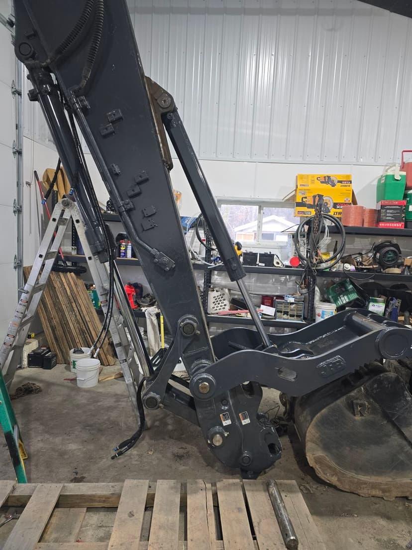 Heavy machinery excavator arm in a workshop with tools and equipment in the background.