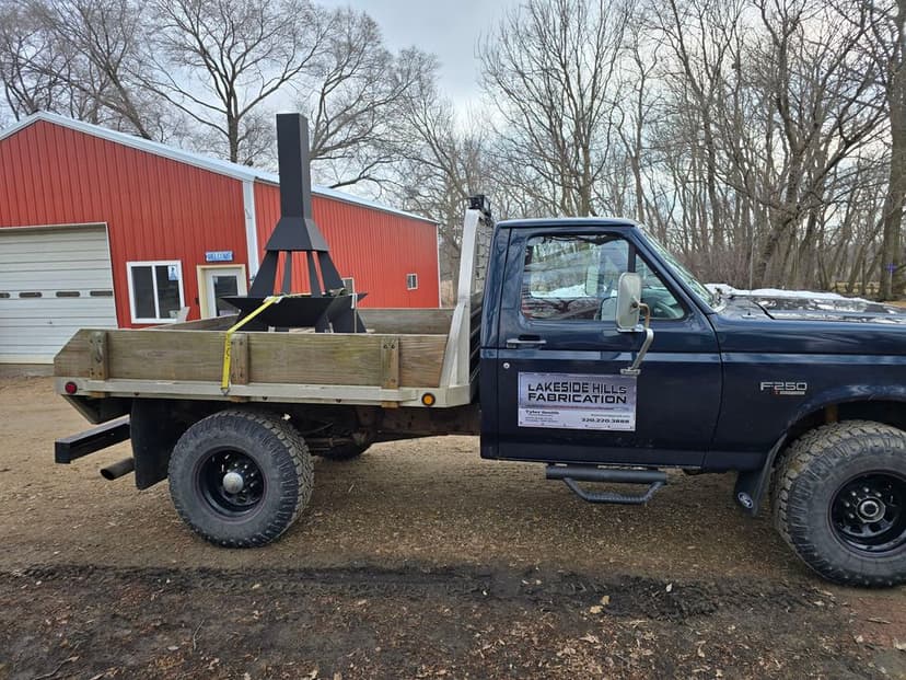 Black pickup truck with wooden bed, marked "Lakeside Hills Fabrication," parked by a red barn.