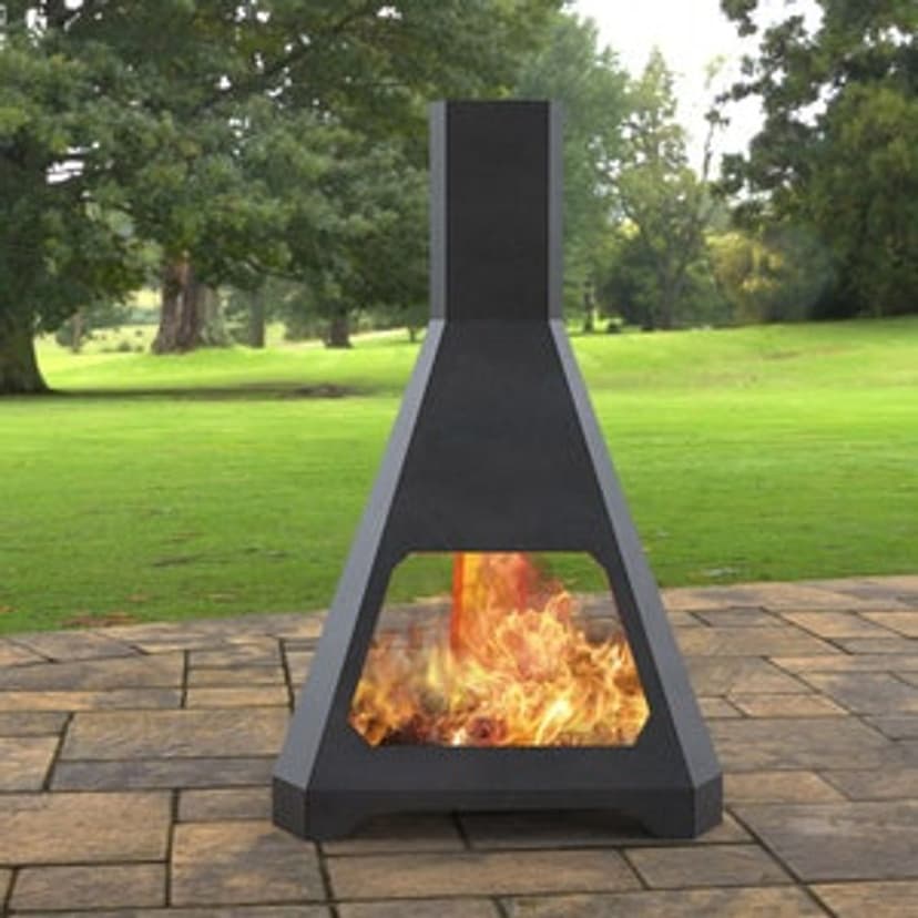 Modern outdoor chiminea with flames, set on a stone patio amidst a green landscape.