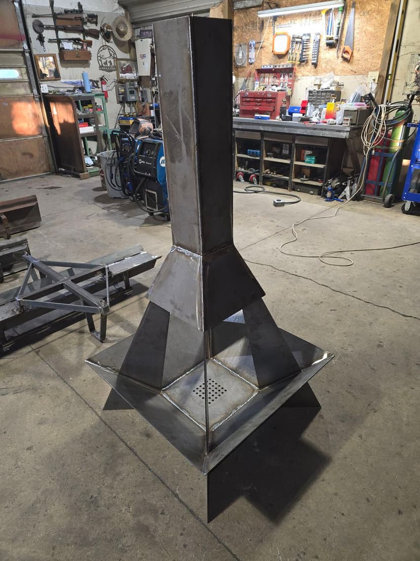 Metal outdoor fire pit on a workshop floor, showcasing a sleek, modern design.