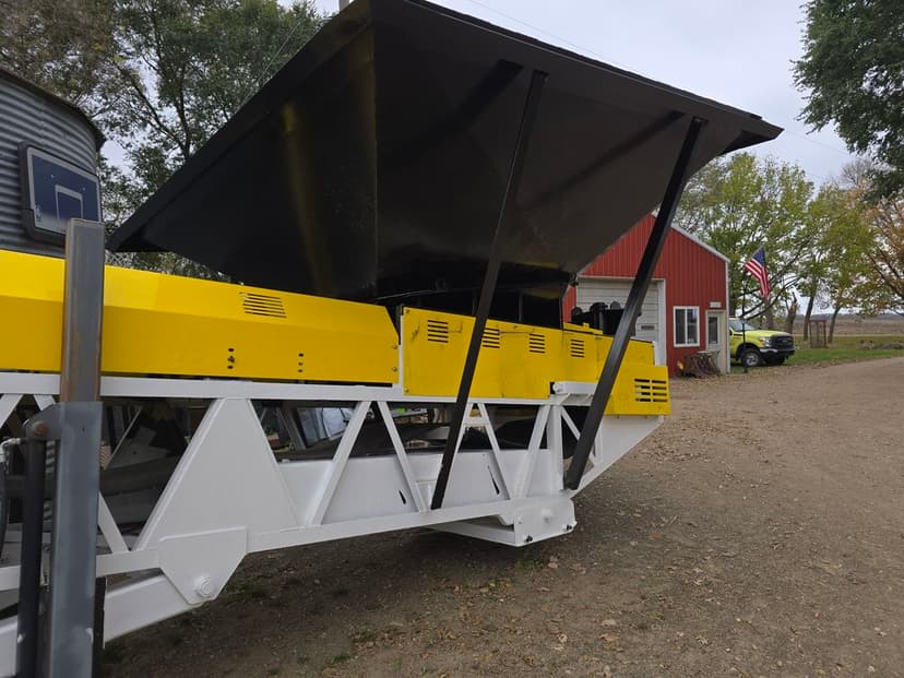 Yellow and black agricultural equipment positioned near a farmstead and American flag.