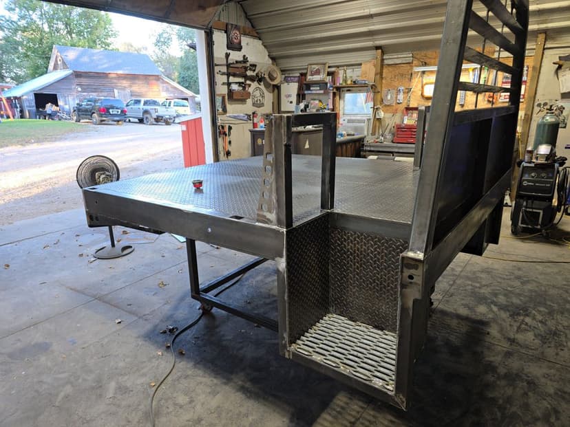 Metal trailer or truck bed with diamond plate flooring in a workshop setting.