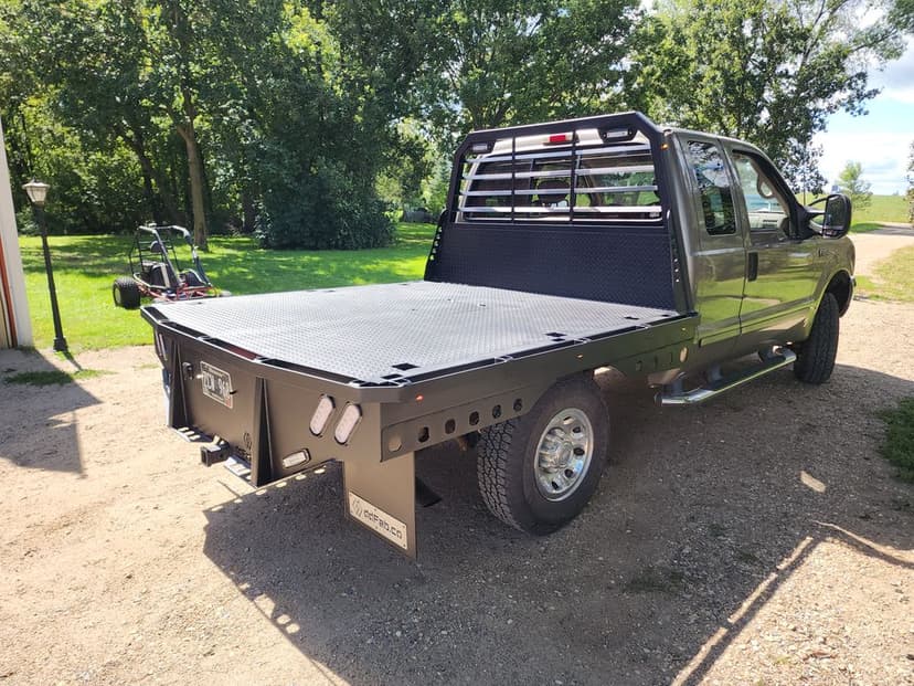 Black pickup truck with flatbed and tool compartments parked on gravel driveway.