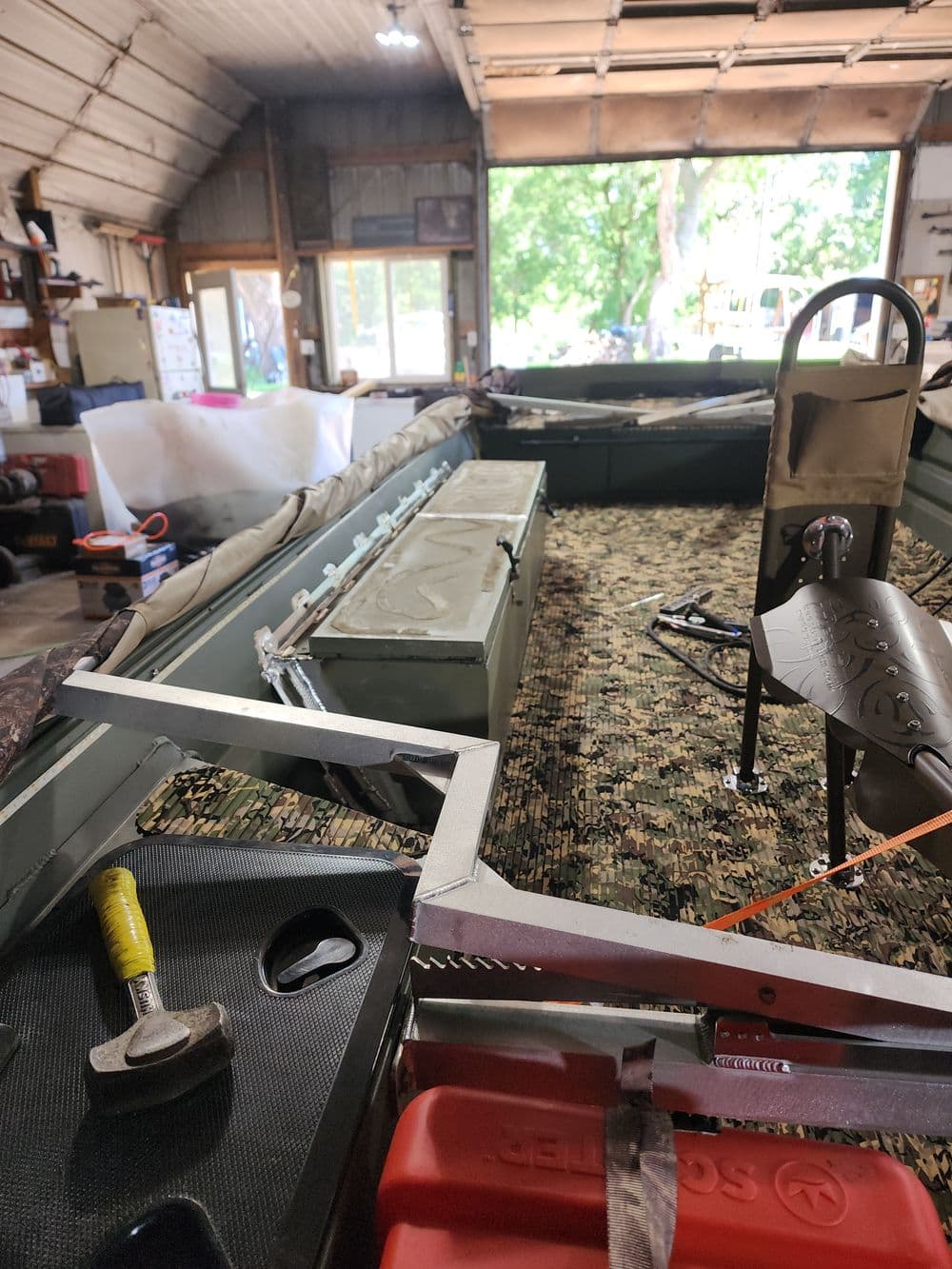 Interior of a boat with camouflage flooring, storage compartments, and a seat in a garage.