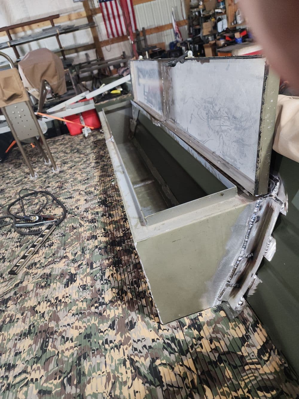 Aluminum storage box for outdoor equipment inside a garage with a camo floor.