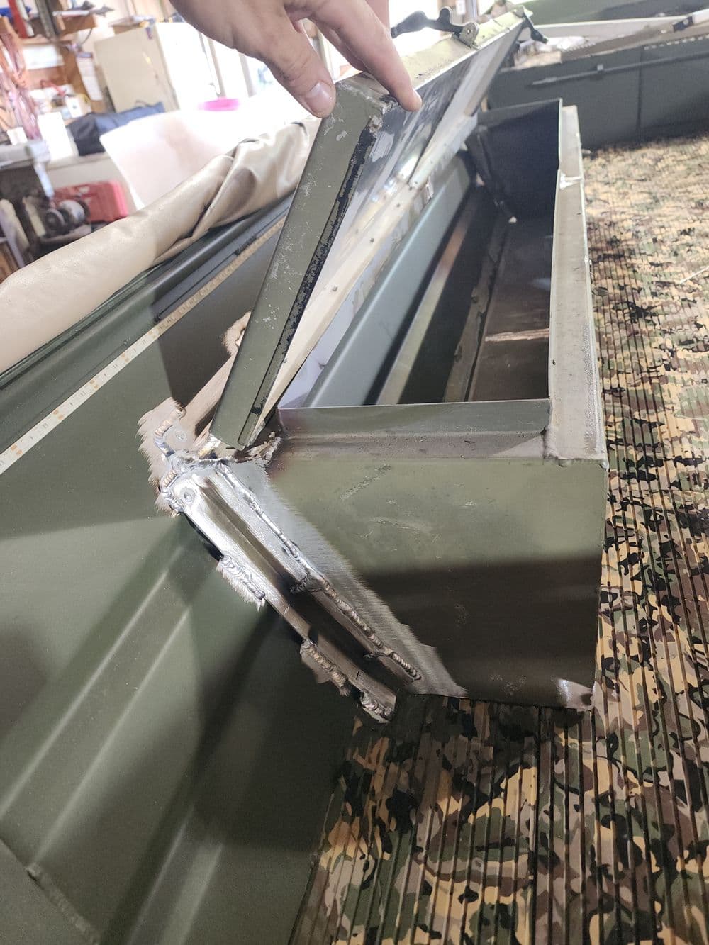 Hand opening a metal storage compartment on a military-style vehicle. Camouflage background.