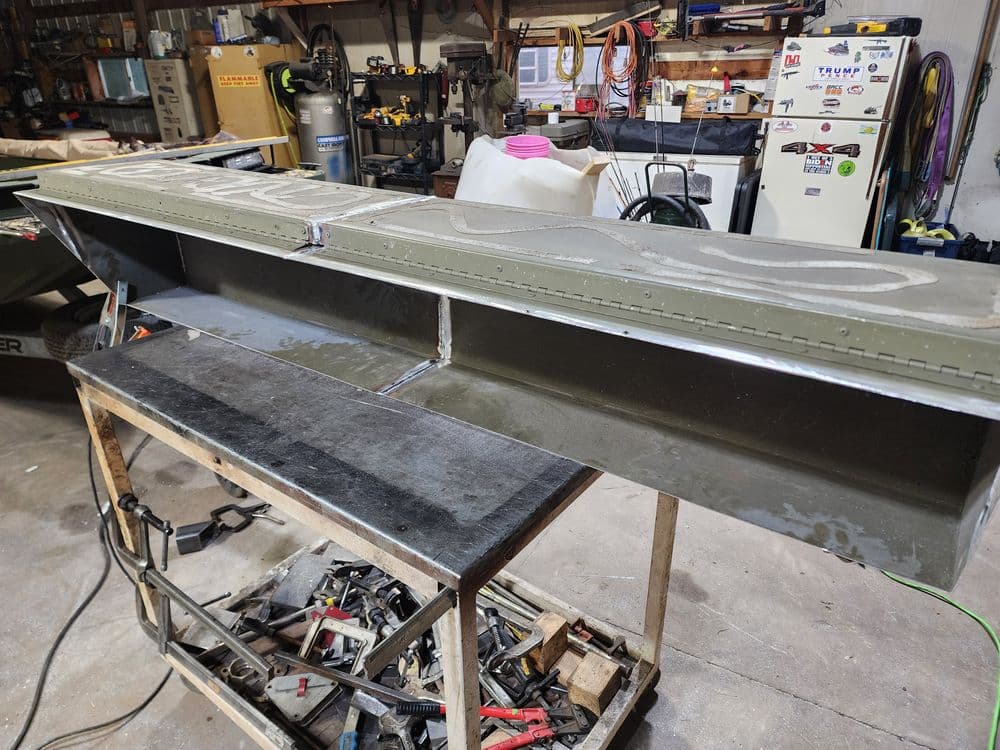 Metalwork project featuring a long, rectangular welded piece on a workbench in a garage workshop.