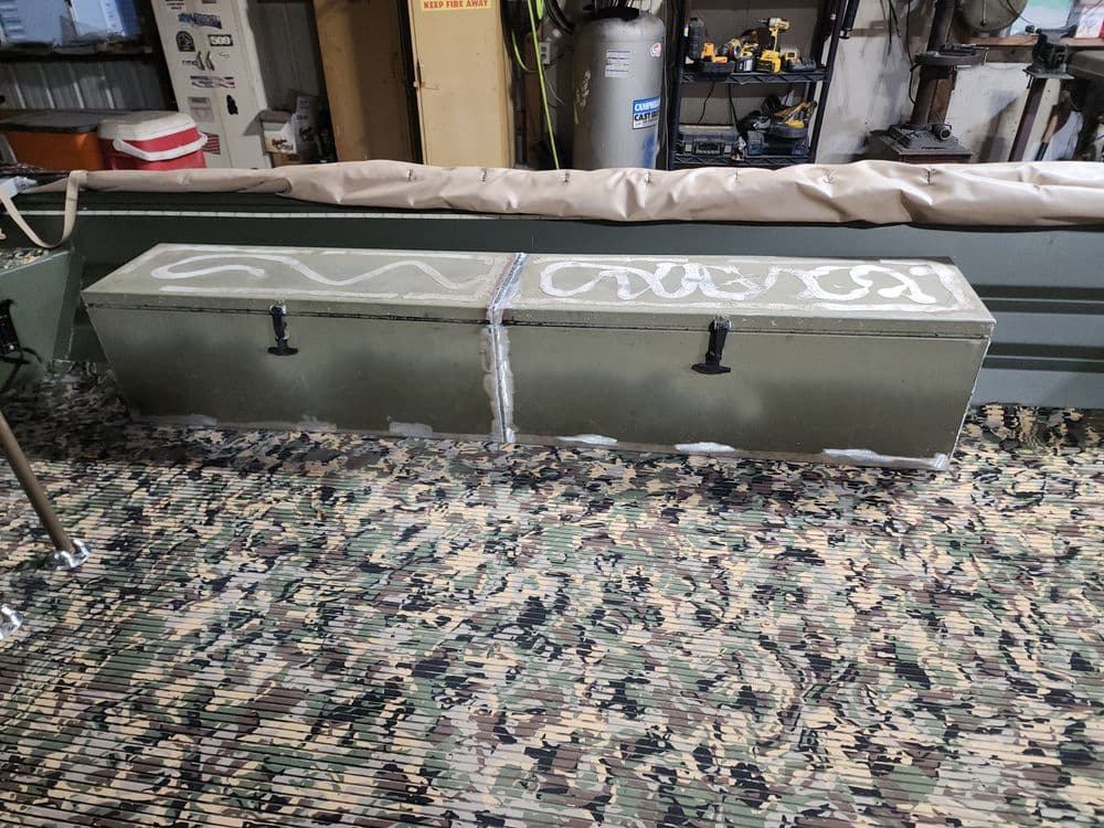 Metal storage box on a camouflaged floor in a workshop setting with tools in the background.