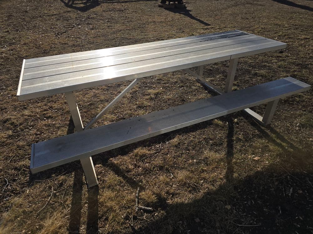 Aluminum picnic table on grass in a park setting, ideal for outdoor gatherings.