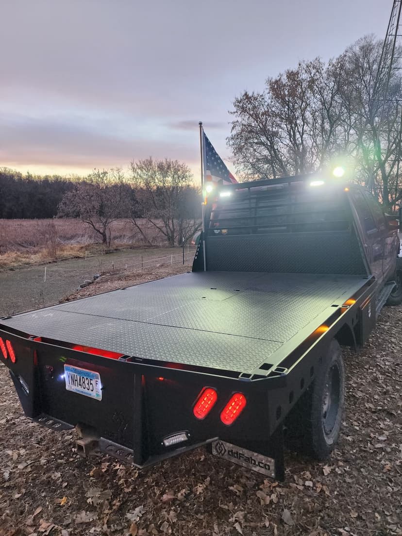 Black flatbed truck with American flag, parked in a rural area at sunset.